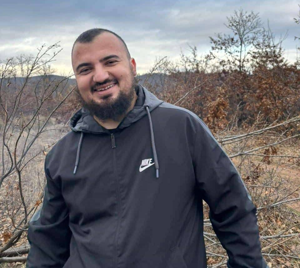 Smiling person in outdoor setting, wearing black Nike jacket.